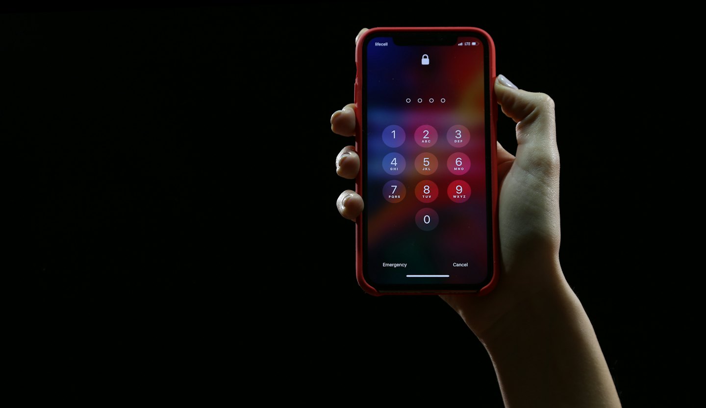 Hand holding a smartphone with passcode entry screen.